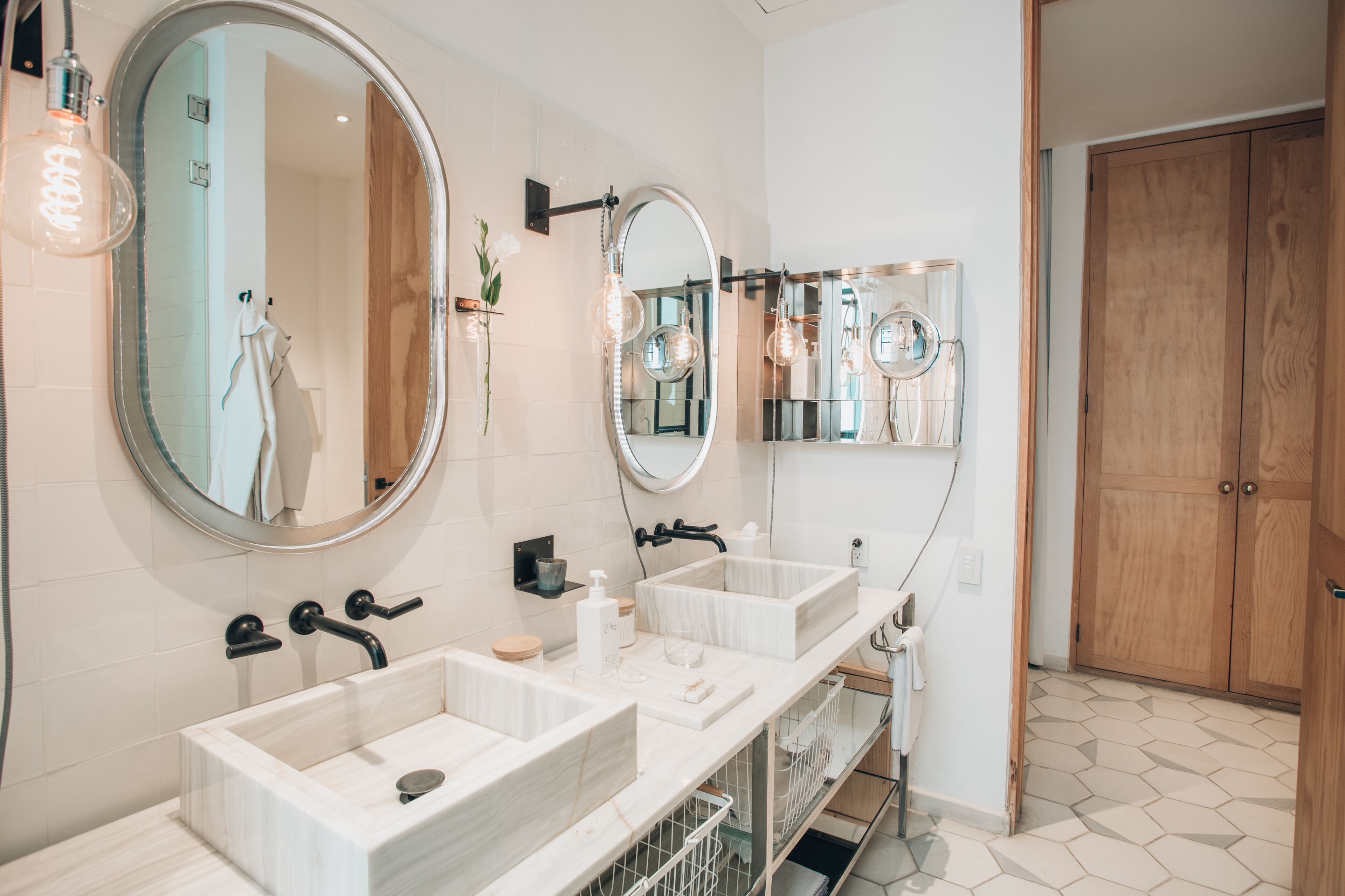 Un baño moderno con dos lavamanos, espejos amplios y un armario de madera.