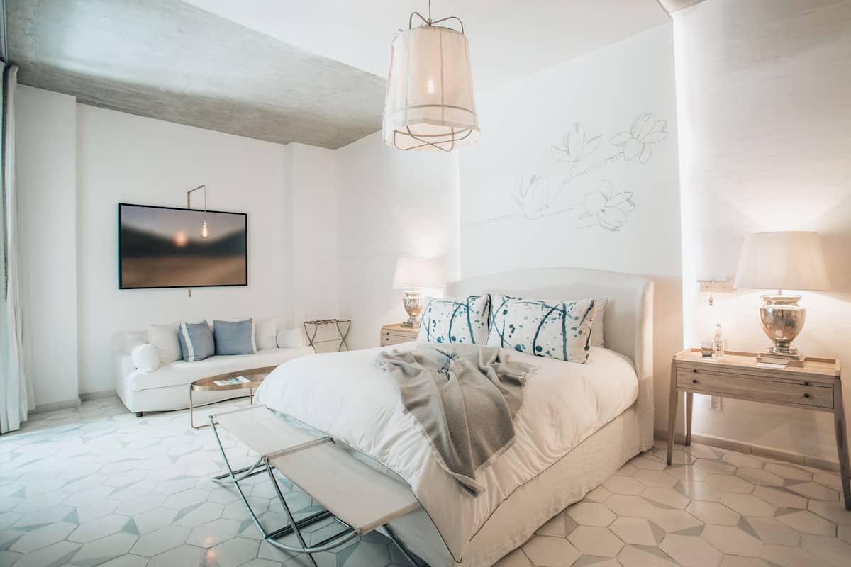 Un dormitorio moderno con cama, sofá, televisor y mesita de noche con lámpara.