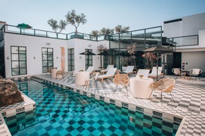 A modern outdoor pool area with lounge chairs and umbrellas, surrounded by a white building with large windows and a glass facade. - LOtel-Casa Arca (San Miguel de Allende)