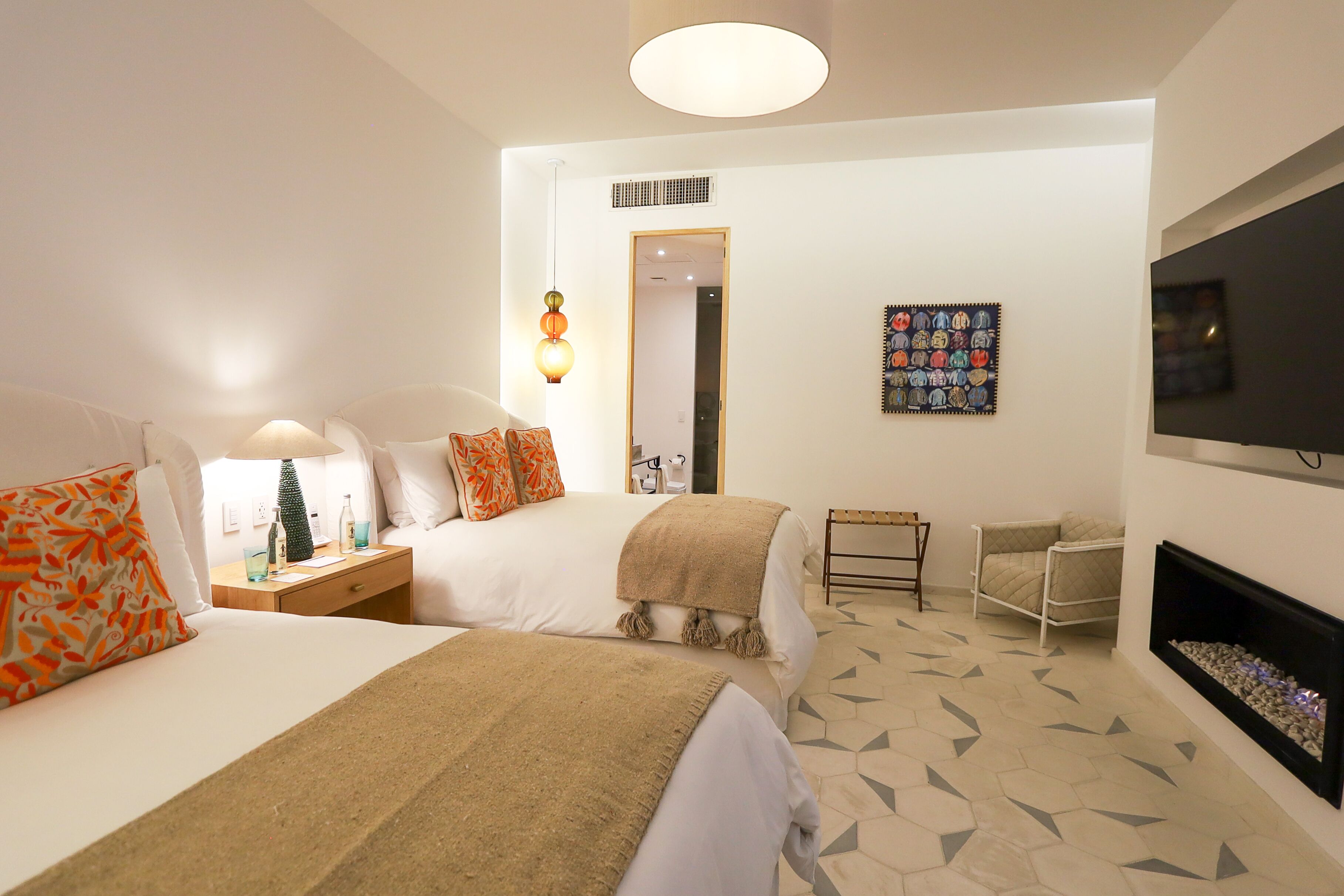 A hotel room with two beds, a television, a fireplace, and a door leading to another room.