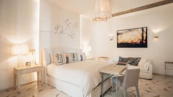 A modern bedroom with a large bed, bedside tables, a desk with a chair, a hanging light fixture, and a wall-mounted abstract painting.