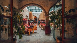 Un interior con arcos de piedra, mesas, sillas y plantas en macetas.