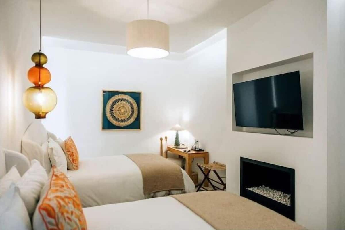 Una habitación de hotel moderna con dos camas, televisión, chimenea y una obra de arte original en la pared.