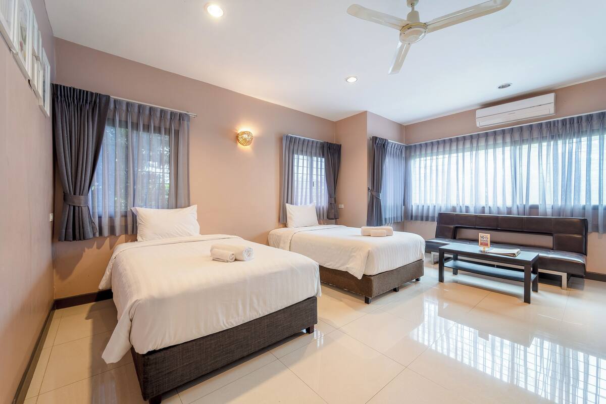 Quarto de hotel com duas camas, um sofá, uma mesa de centro e um ventilador de teto.