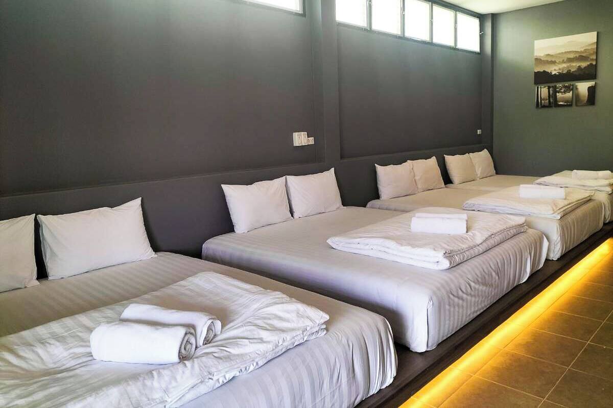 Quarto de hotel com quatro camas dispostas em linha, cada uma com lençóis e almofadas brancas.