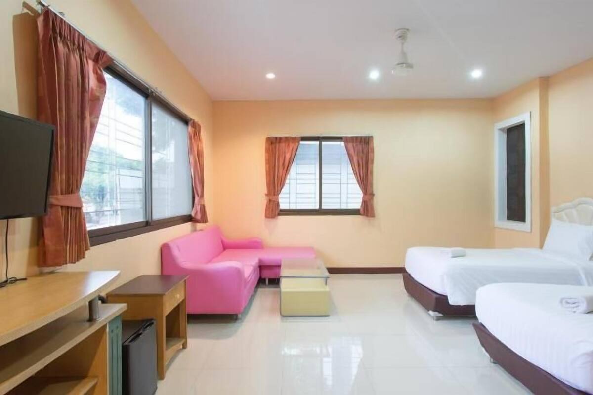 Quarto de hotel com televisão, sofá rosa, duas camas e janela com cortinas.