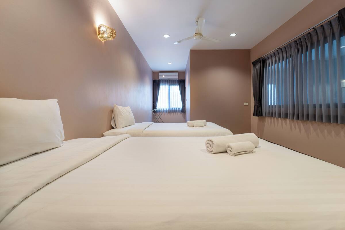 Quarto de hotel com duas camas, um ventilador de teto e uma janela com cortinas.