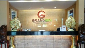 A reception desk at Grand Sir hotel's Resort Khaoyai with a wooden backdrop, two decorative peacock statues, and a logo.