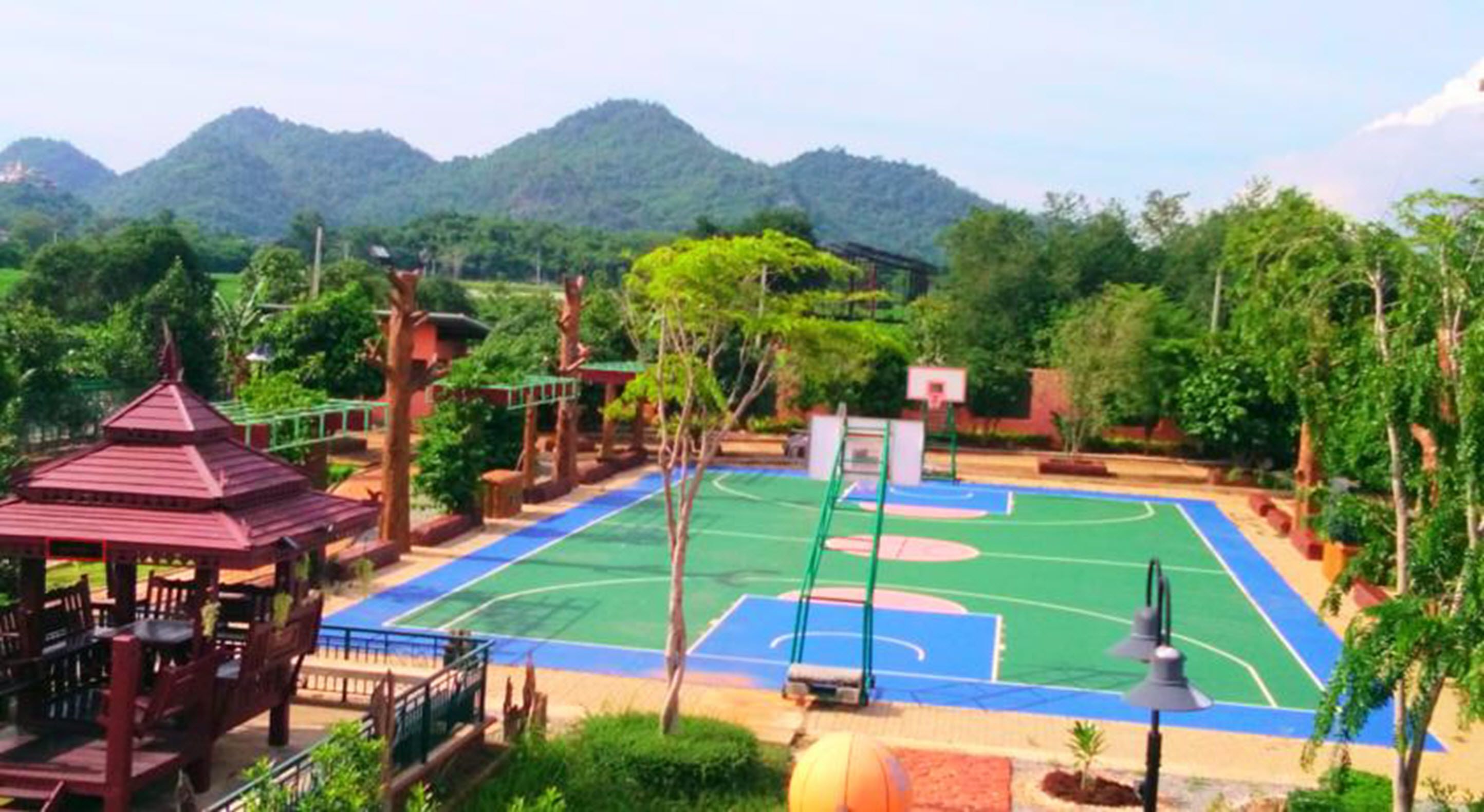 Un terrain de basket entouré de verdure et un pavillon.