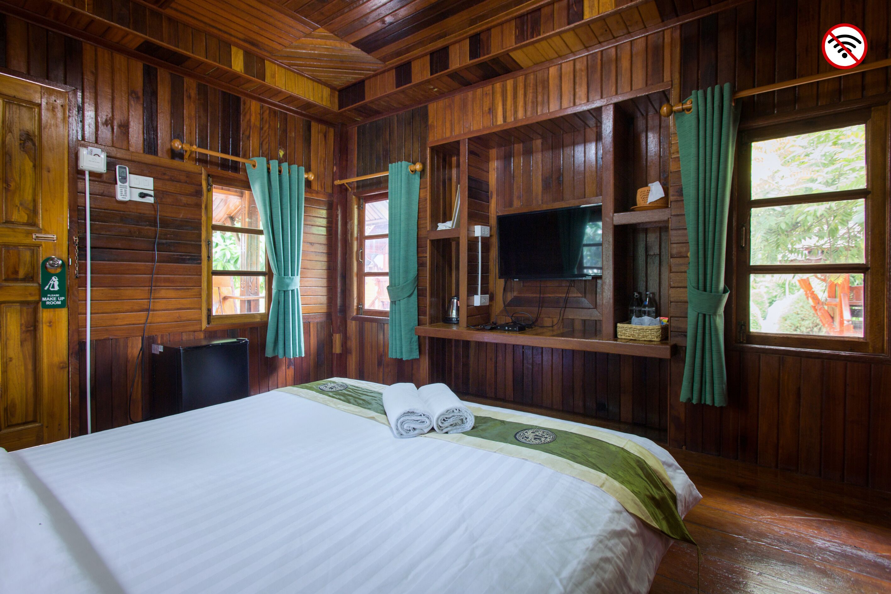 Una habitación con piso de madera, una cama, un televisor y una ventana con cortinas.