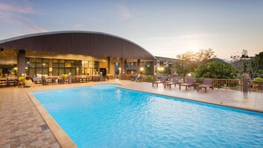 A swimming pool with a curved building in the background, outdoor seating, and a landscaped area.