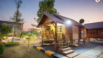 A wooden cabin with a porch and steps, surrounded by a landscaped garden with trees and a pathway.