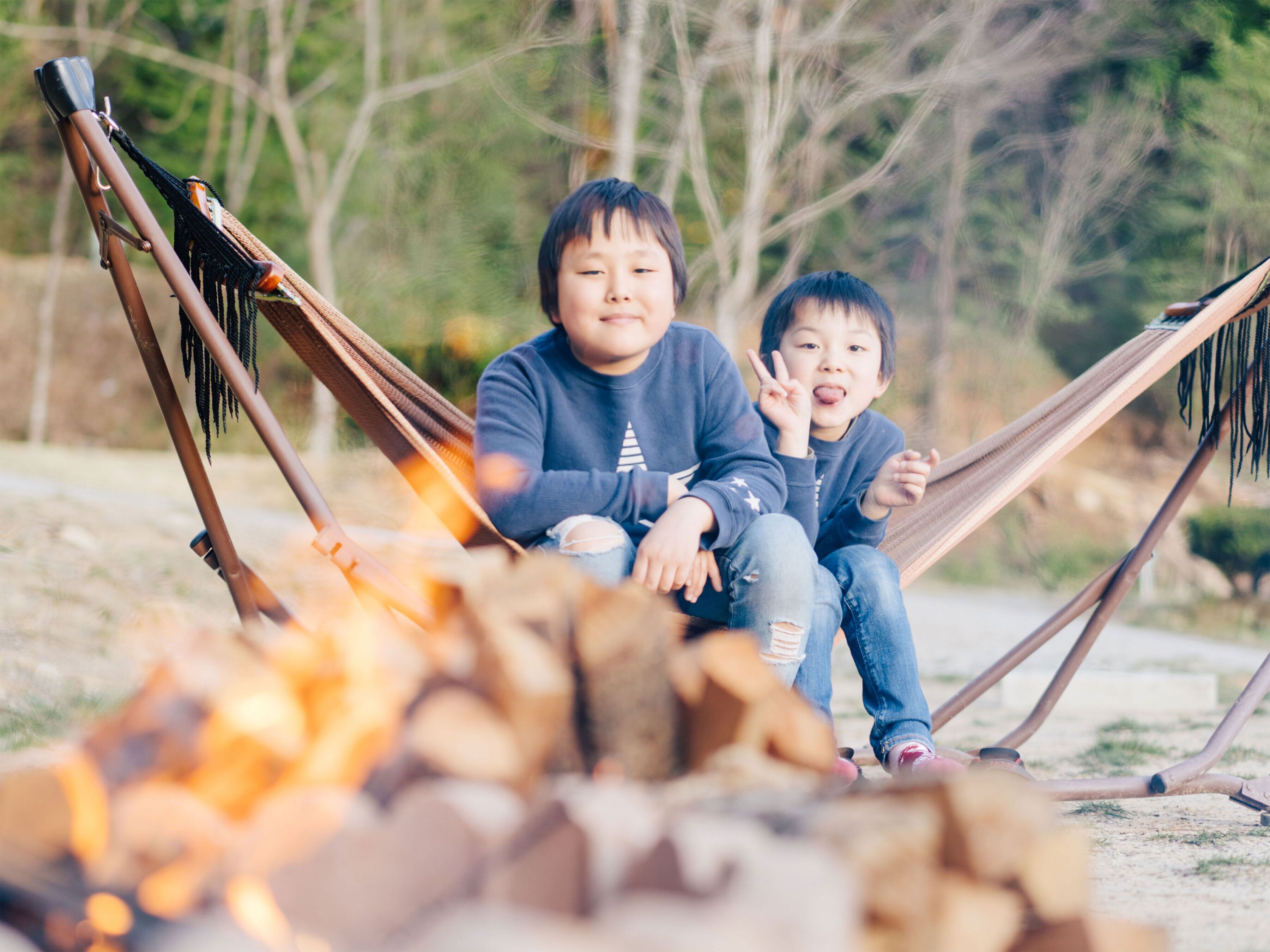 Two people sitting on a hammock over a campfire.