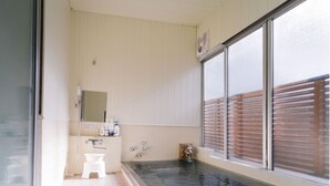 Une salle de bain avec une grande baignoire, des toilettes et une fenêtre avec des stores.