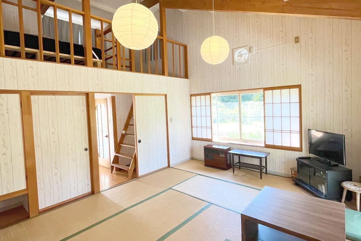 A traditional Japanese-style room with tatami flooring, a television, a radio, and a staircase leading to an upper level.