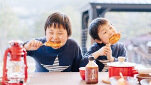 Deux enfants sont assis à une table et mangent. Sur la table, on peut voir une lanterne, une bouteille et un pot rouge.