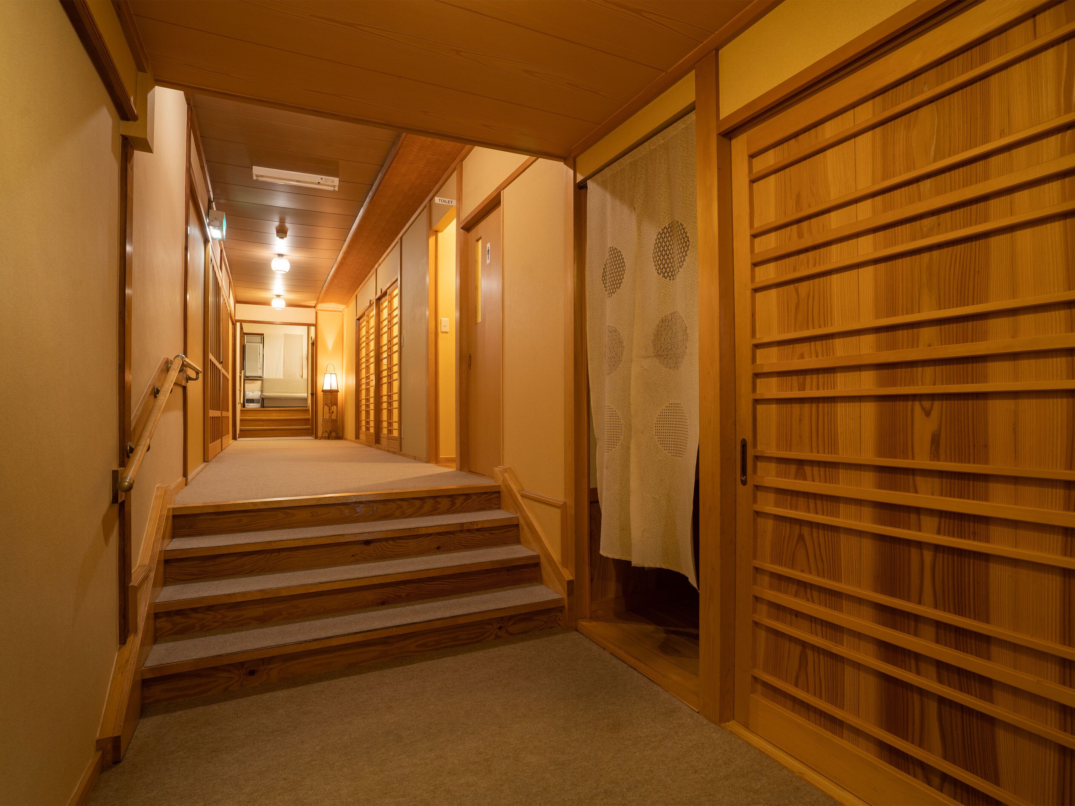 A wooden interior hallway with a carpeted staircase leading to a room.