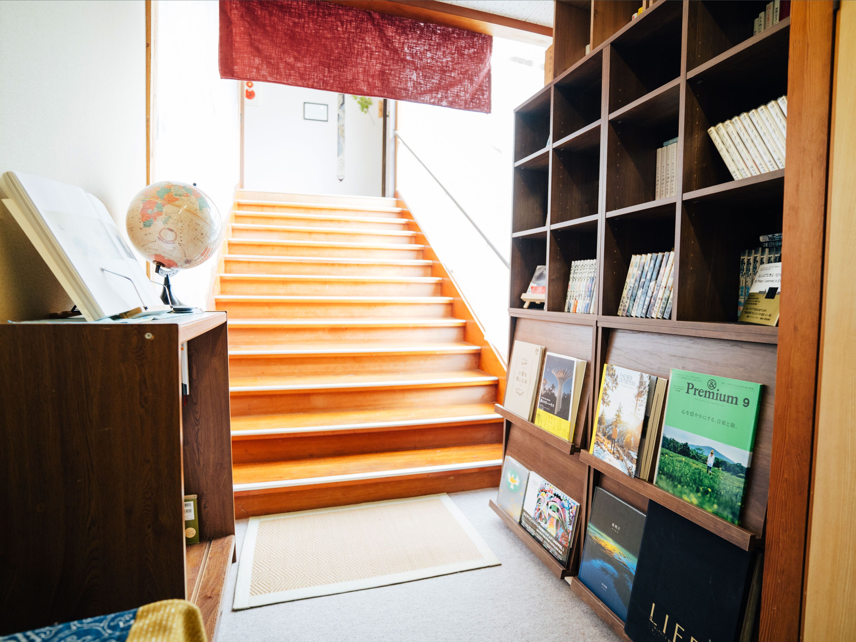 Uma escada leva a um patamar com uma estante de madeira repleta de livros e quadros emoldurados.