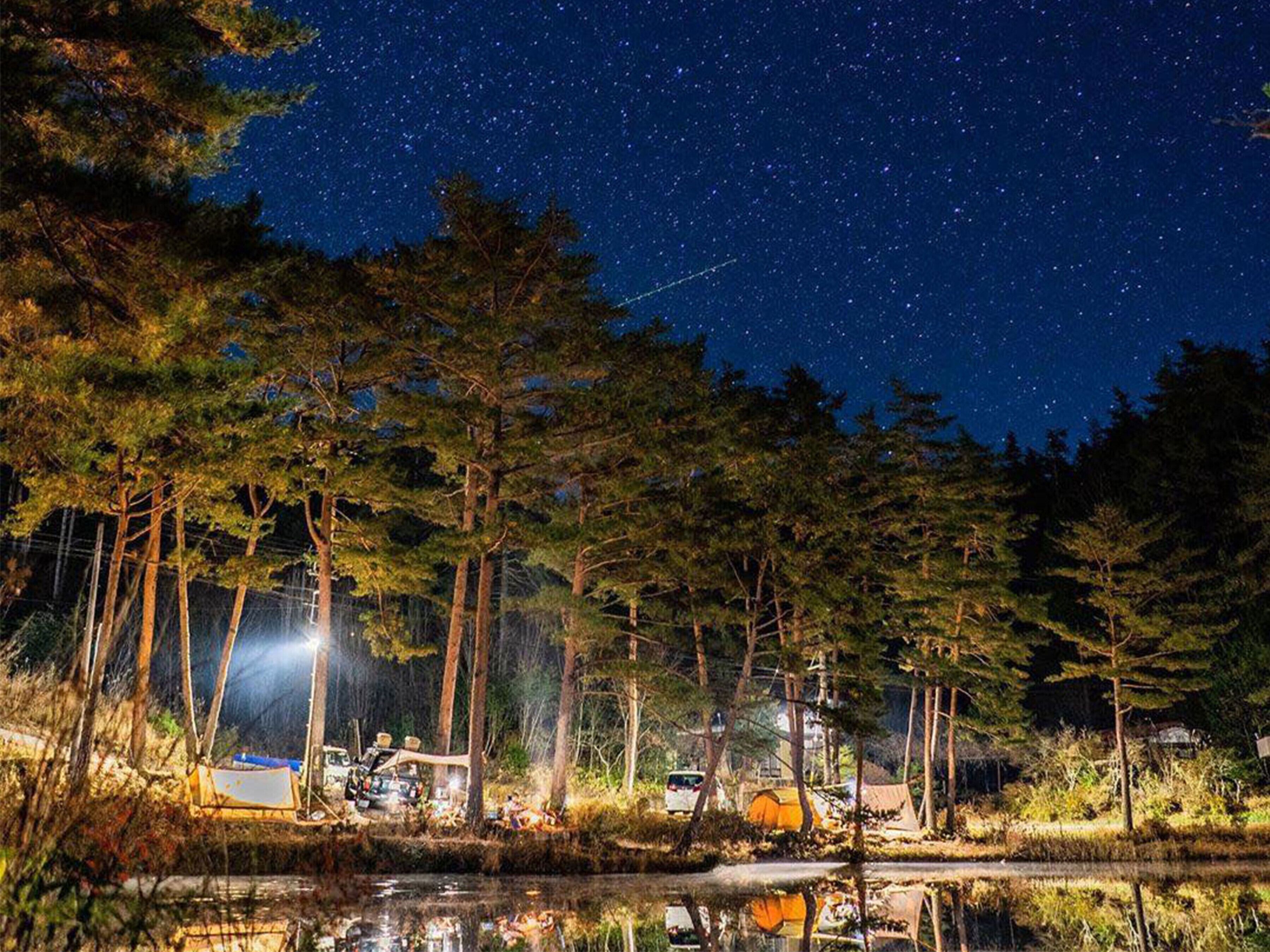 A campsite with tents and a vehicle by a lake at night under a starry sky.