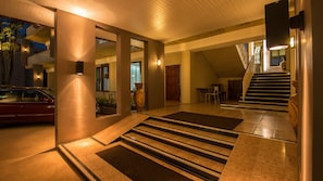 Un hall d’hôtel avec une voiture garée à l’extérieur, un escalier et un comptoir d’accueil.