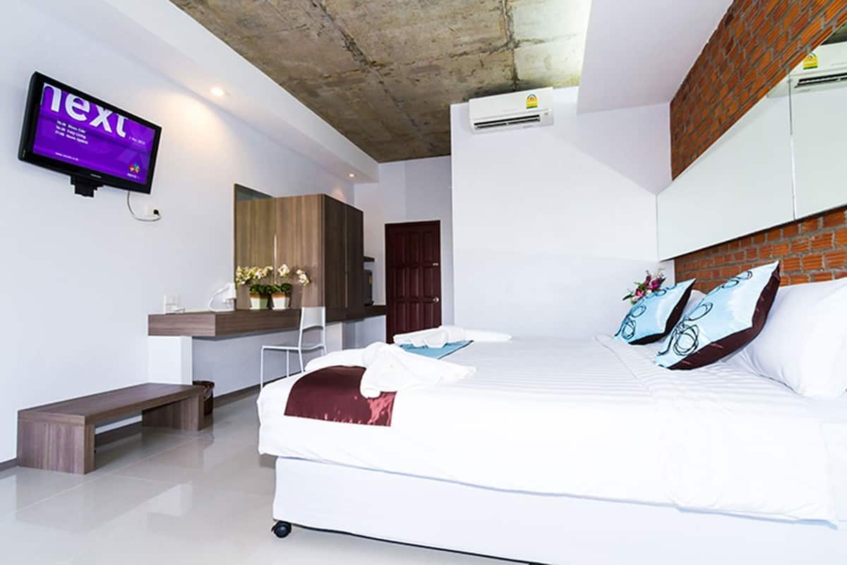 A modern hotel room with a bed, a desk, a chair, a TV, and an air conditioning unit.