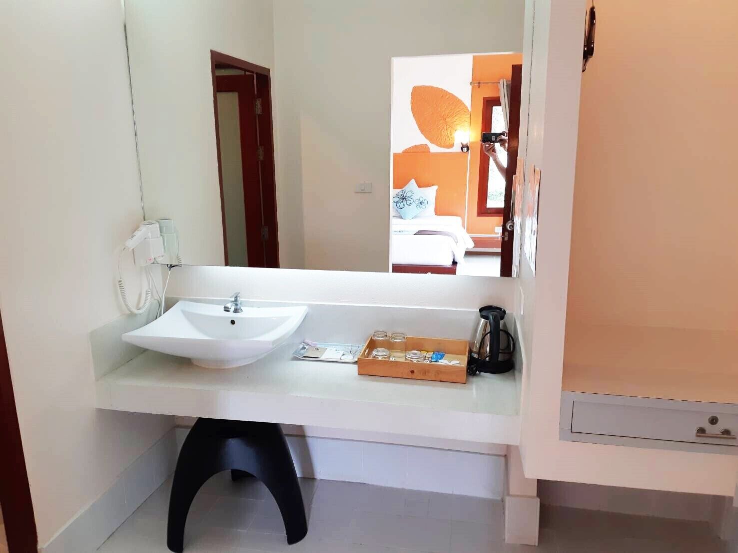 Un baño con lavamanos blanco, espejo, secador de pelo y cafetera.