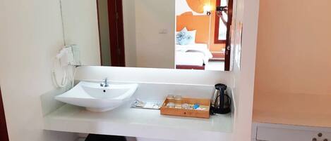 Un baño con lavamanos blanco, espejo, secador de pelo y cafetera.
