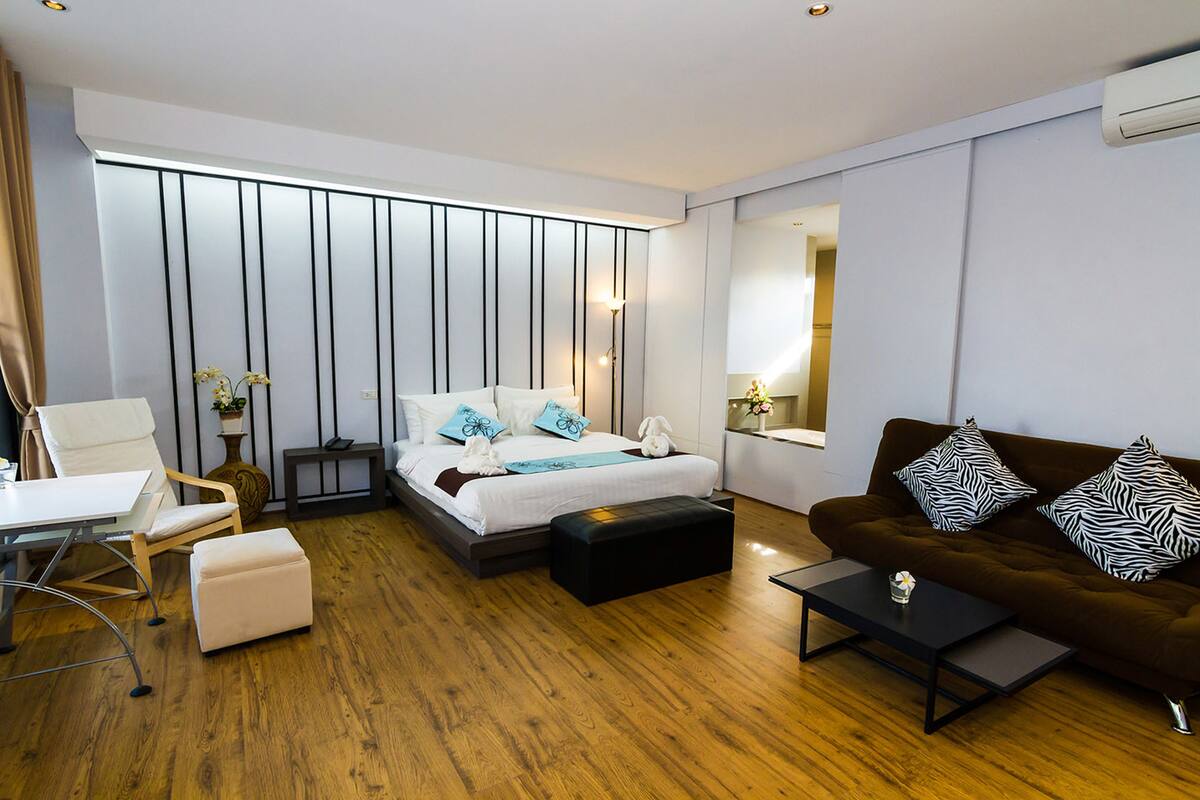 A modern hotel room with a bed, a sofa, a coffee table, a desk, and a chair.