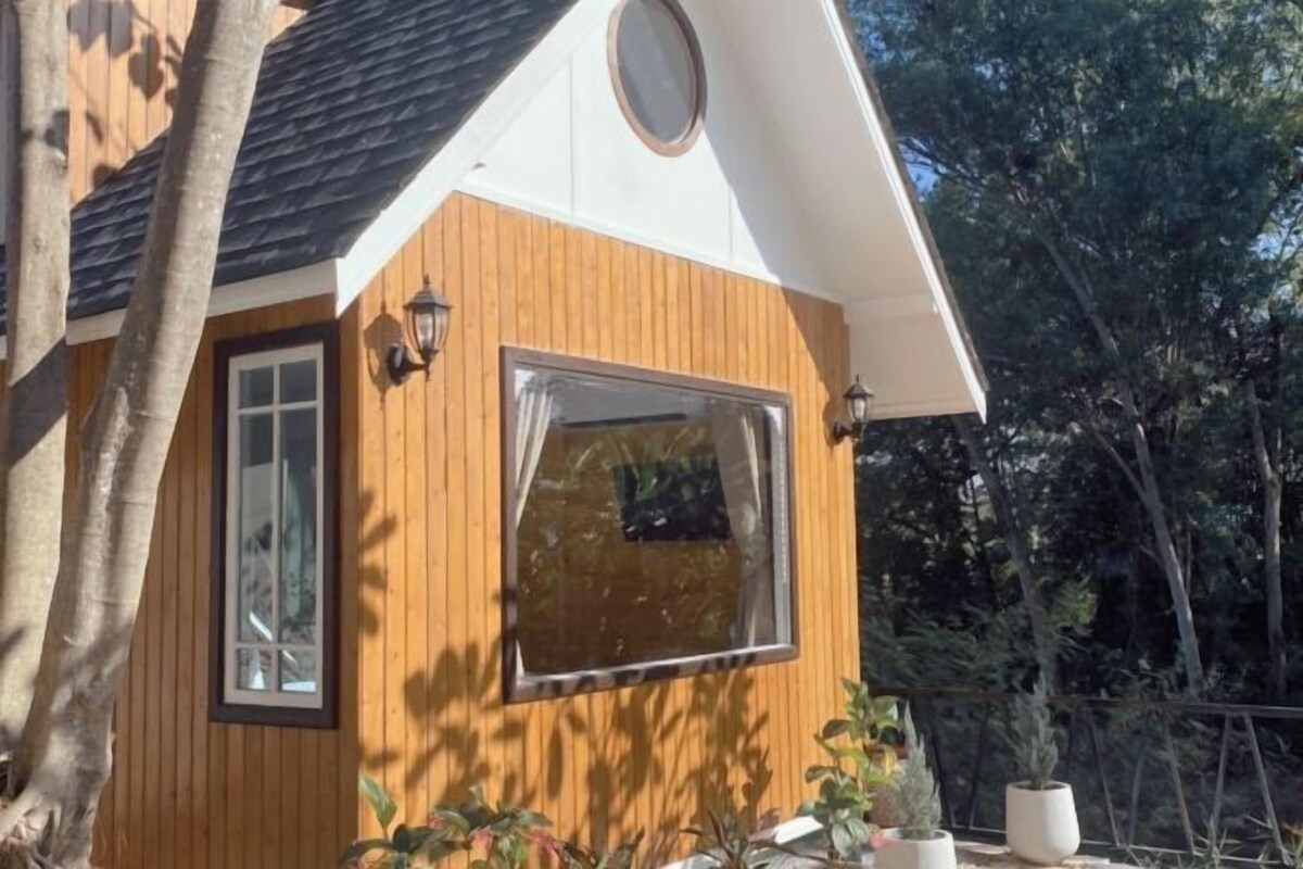 Une cabane en bois avec une grande fenêtre, une porte et une petite fenêtre circulaire sur le toit.