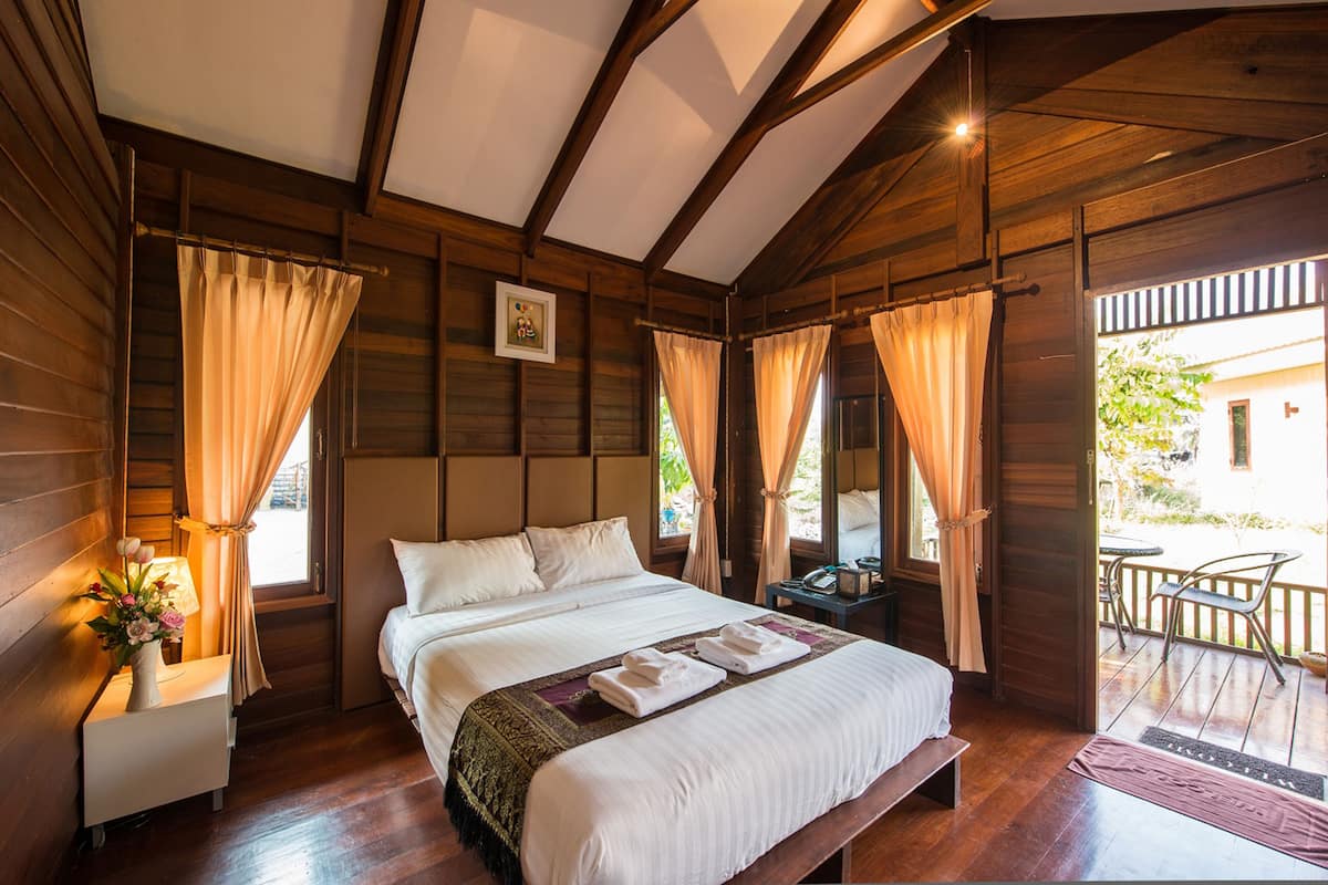 A wooden cabin-style bedroom with a large bed, a nightstand with a lamp, and a view of the outside balcony.