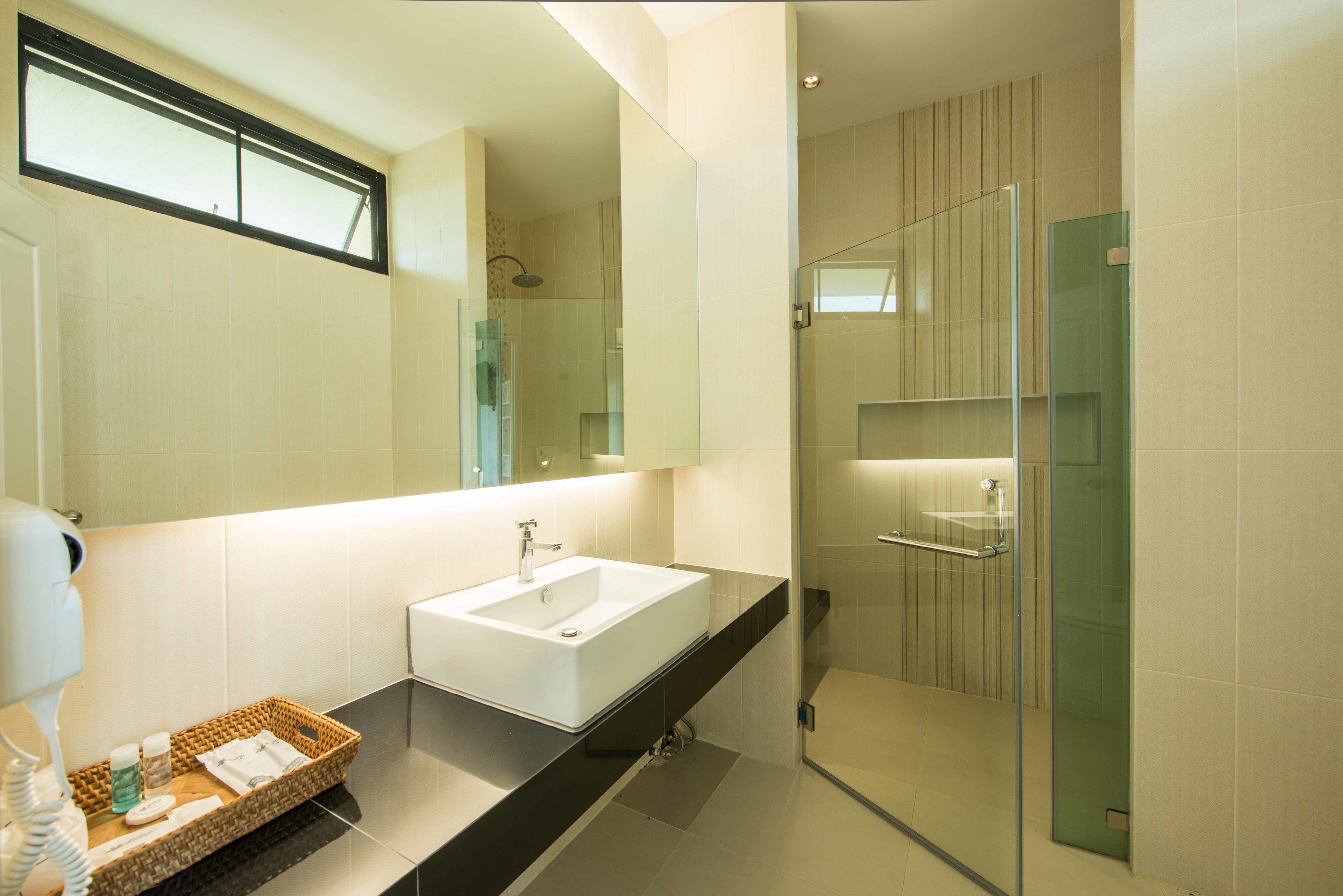 Un baño moderno con un espejo grande, un lavamanos blanco y una ducha con mampara de vidrio.
