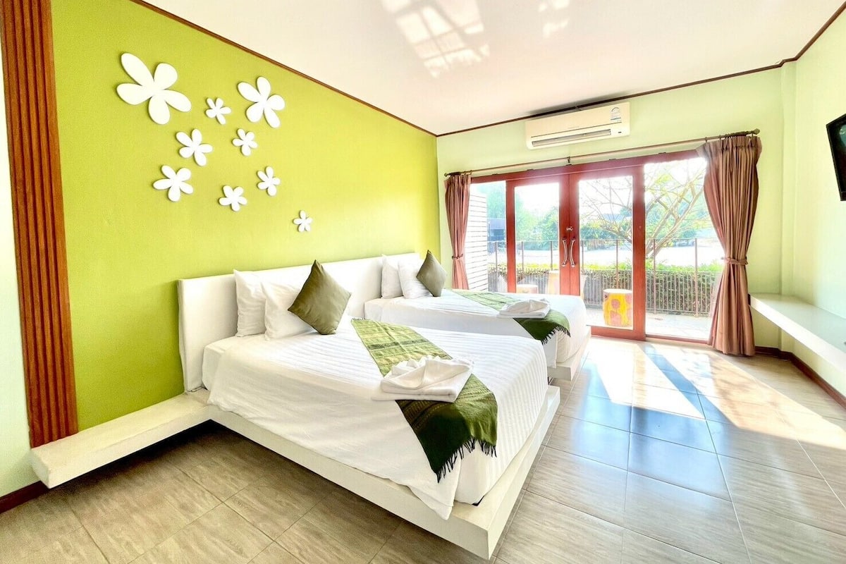 A hotel room with a bed, a window with curtains, a wall with decorative flowers, and a balcony.