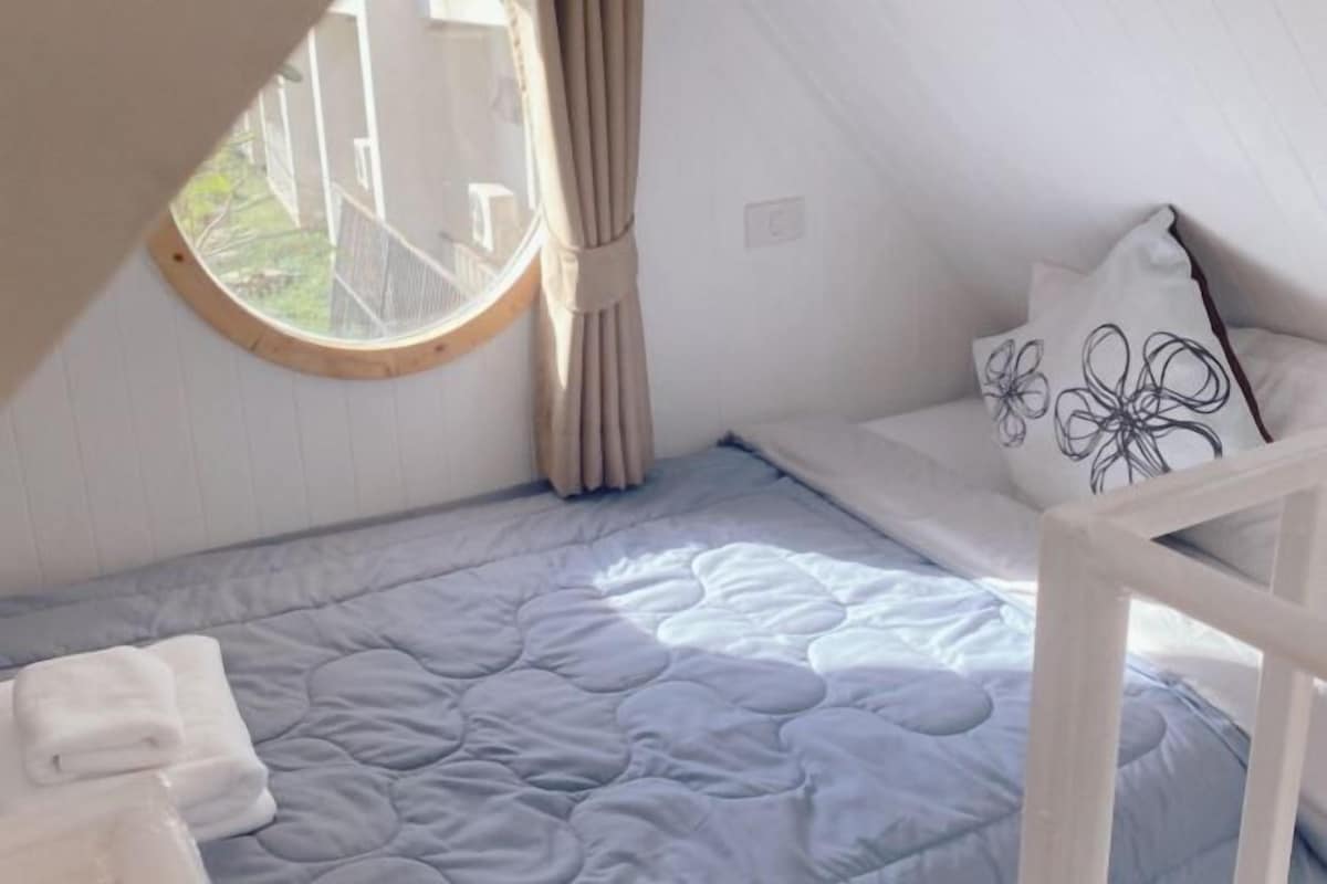 Ein kleiner, gemütlicher Raum mit einem Etagenbett, einem Rundfenster und Blick ins Freie.