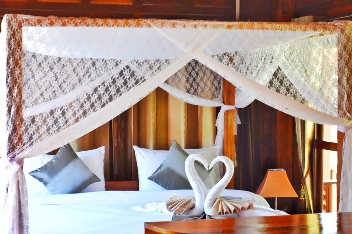 A bed with a canopy, pillows, and a swan-shaped towel arrangement.