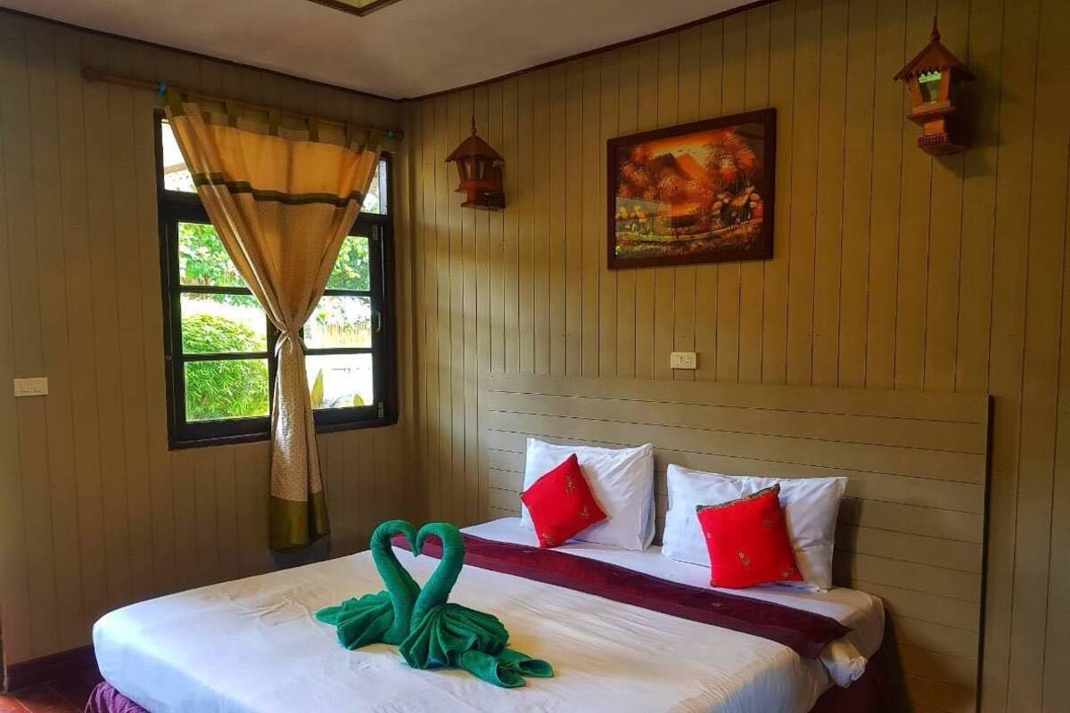 A hotel room with a bed, two red pillows, a green towel, a painting, and two wall-mounted lanterns.