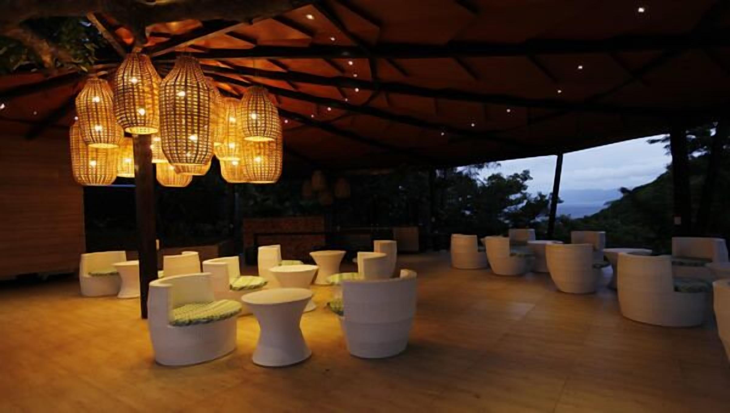 Zona relax esterna coperta, con mobili bianchi moderni e lampade in vimini appese.