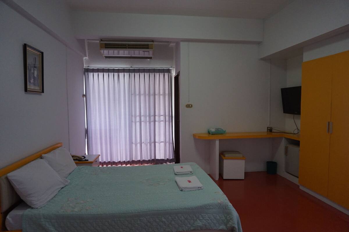 Un dormitorio con cama, escritorio, televisión y aire acondicionado.