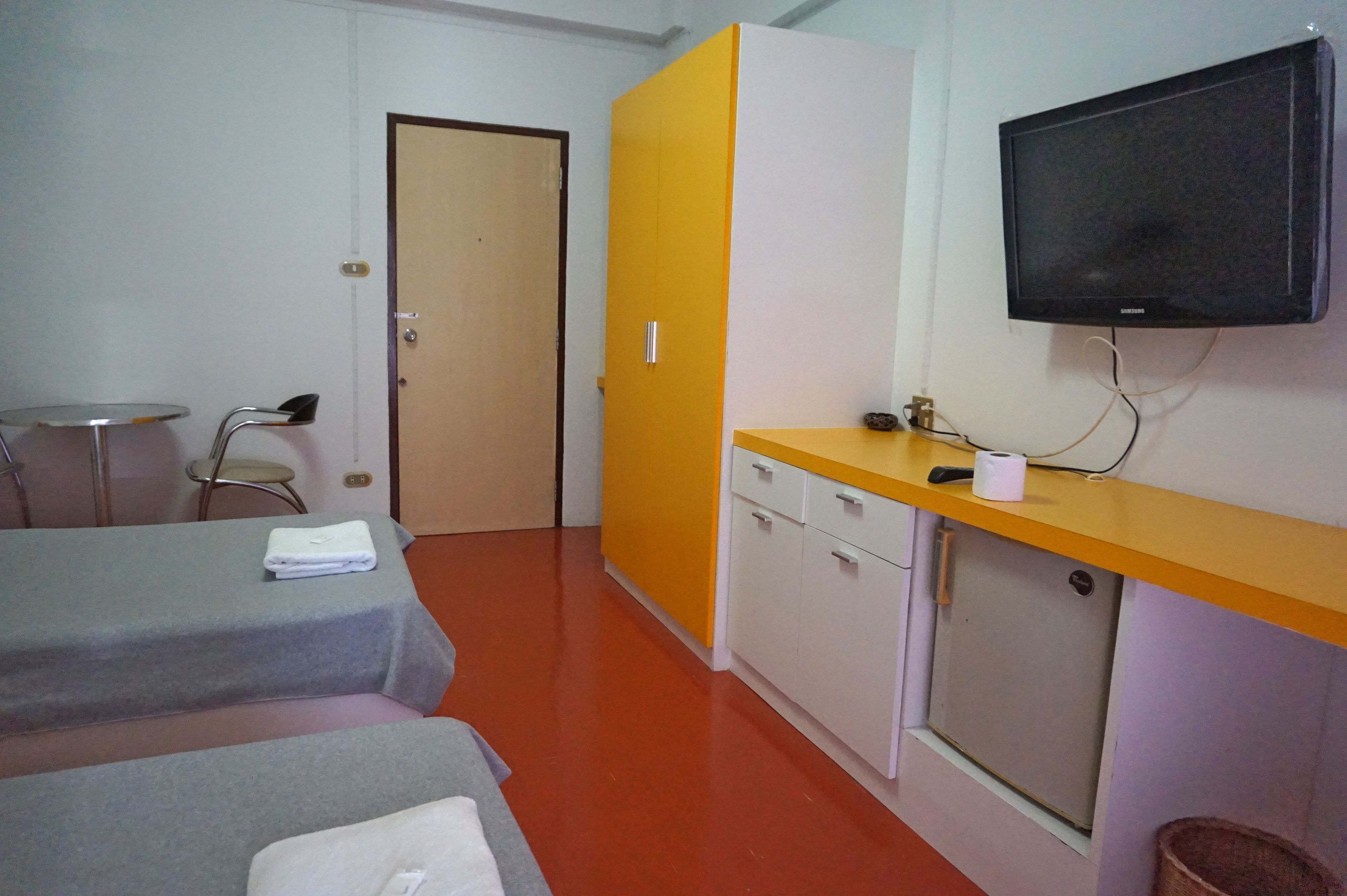 A hotel room with two beds, a small table, a chair, a wardrobe, a television, and a window.