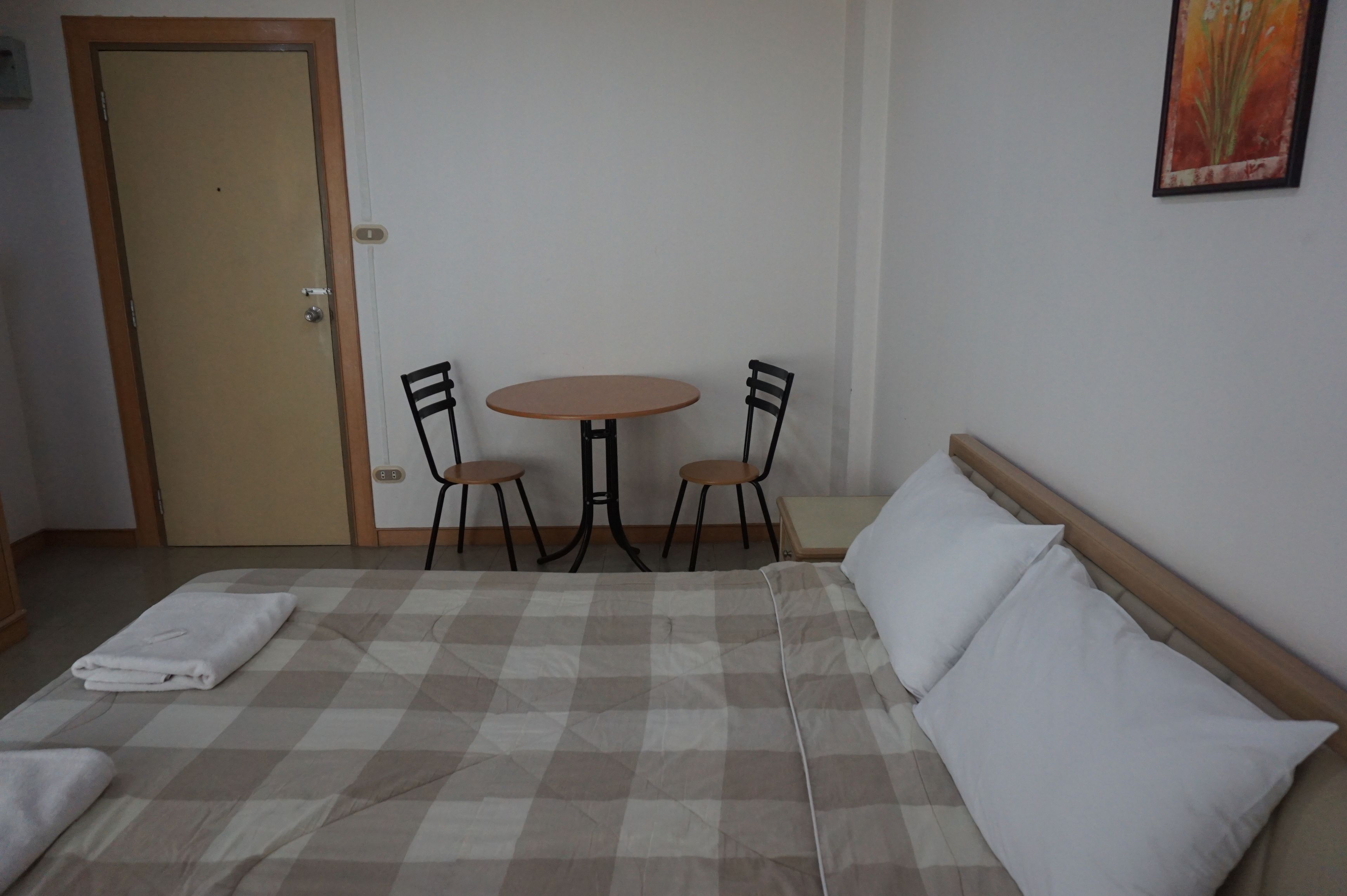 Quarto com cama, duas cadeiras, uma mesa pequena e uma porta.