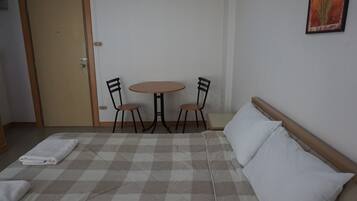 Quarto com cama, duas cadeiras, uma mesa pequena e uma porta.