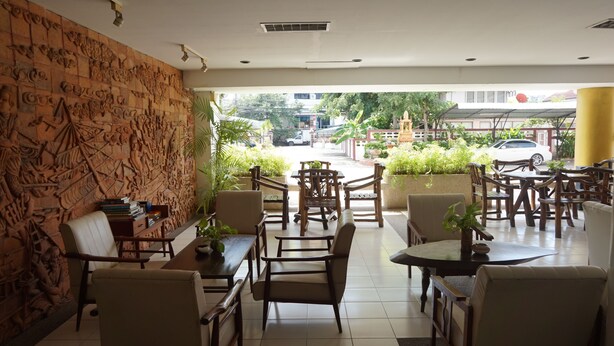 A hotel lobby with a large, intricately carved wall, multiple seating areas with tables and chairs, and a view of the street outside.