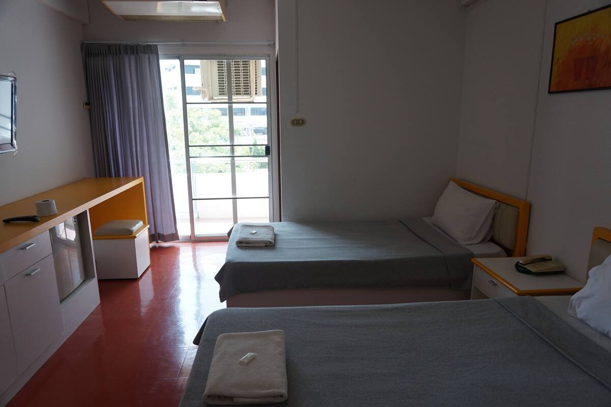 Habitación de hotel con dos camas, un escritorio, una silla, una mesita y una ventana con cortinas.