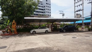 A parking area with two cars, a covered shelter, and a decorative statue.