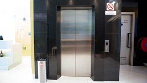 Un ascensor con pantalla digital, un cubo de basura y un cartel de prohibido fumar.