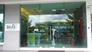 Entrada de un edificio moderno con fachada de vidrio, un cartel que dice "IN8 BINTULU", y una calle visible con automóviles y un paso de peatones.