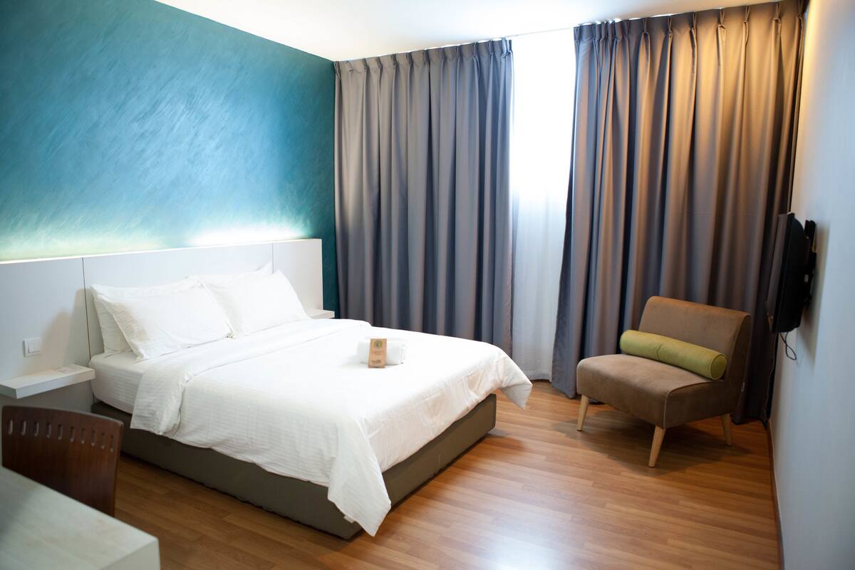 Una habitación de hotel moderna con una cama, una silla, un televisor y una ventana con cortinas.