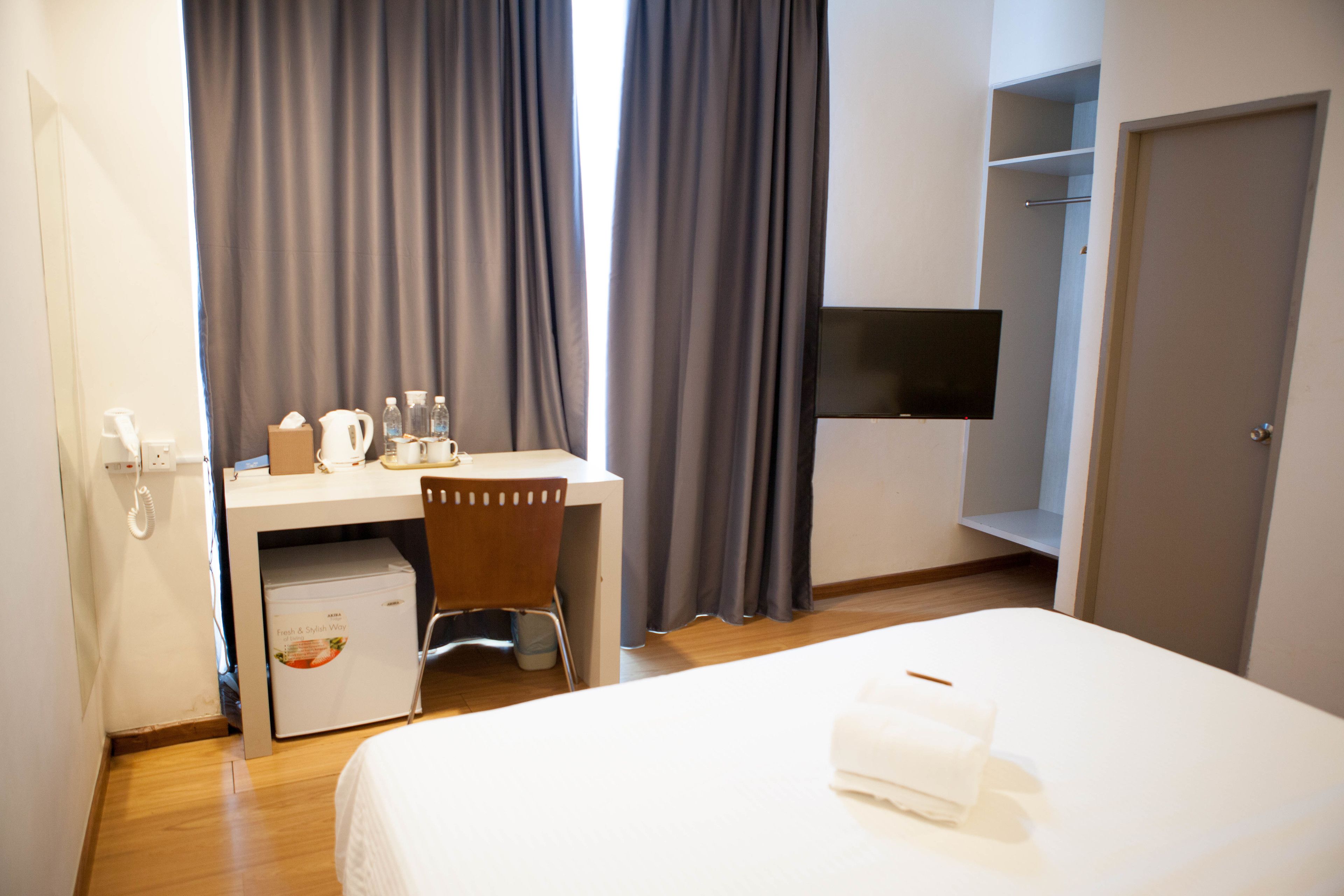 A hotel room with a bed, a desk with a chair, a small refrigerator, a flat-screen TV, and a wardrobe.