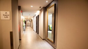 Pasillo de hotel con un cartel que indica un ascensor para huéspedes, puertas a la derecha y una planta en el centro.