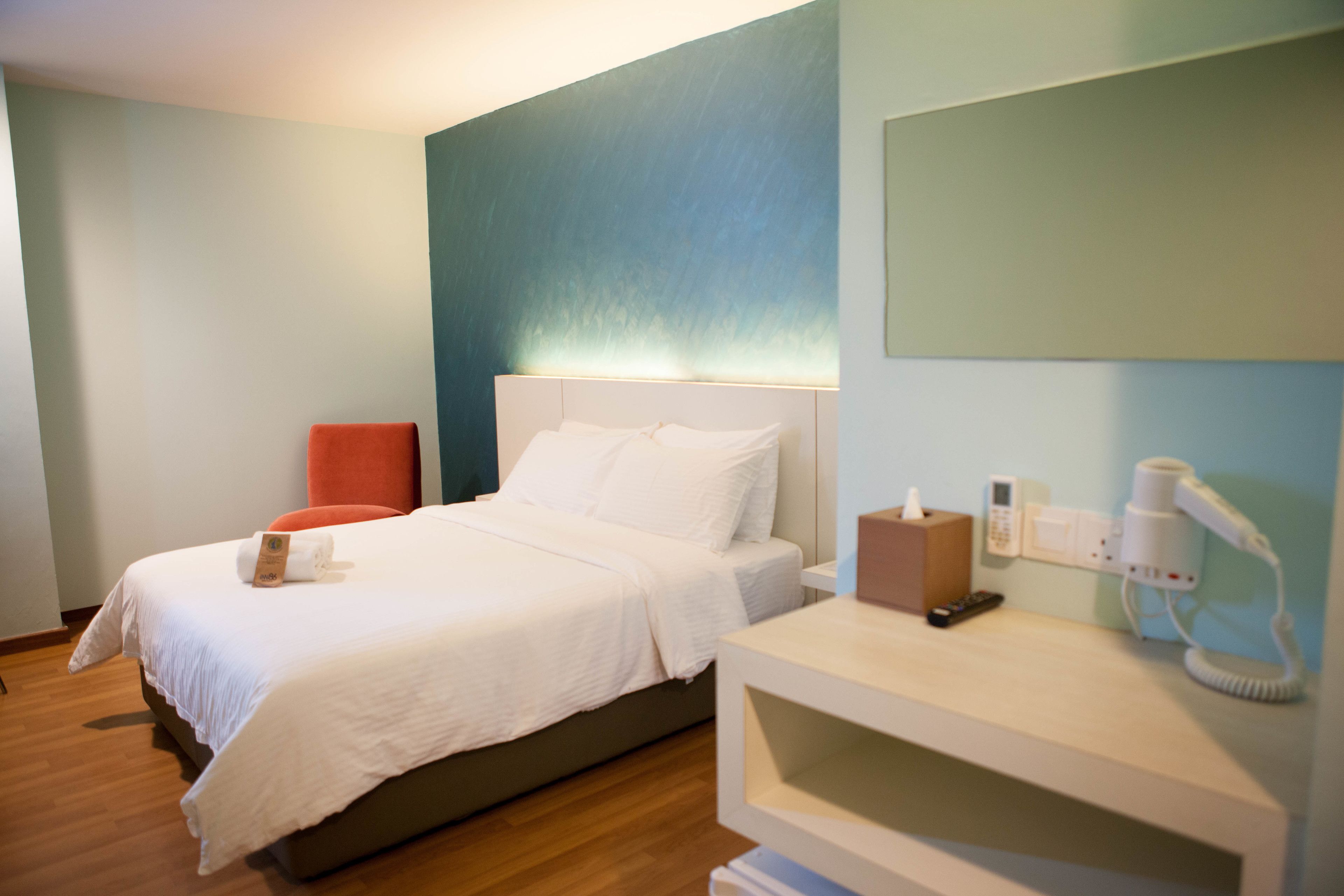 Una habitación de hotel con una cama, una mesita de noche con lámpara, teléfono y secador de pelo.