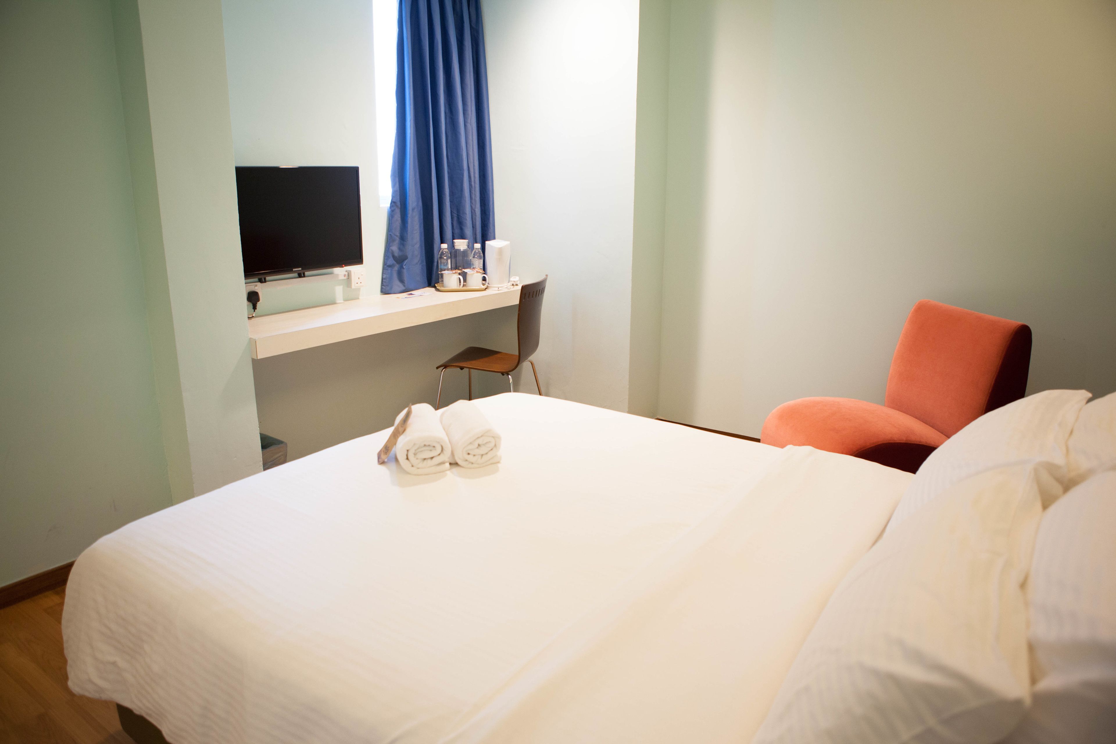 A hotel room with a bed, a TV, a desk with a computer, and a chair.